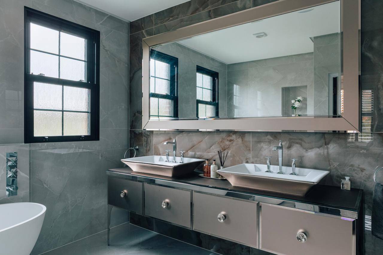Luxury grey stone bathroom vanity with double vessel sinks, large mirror, and black window frames, Love Locations.