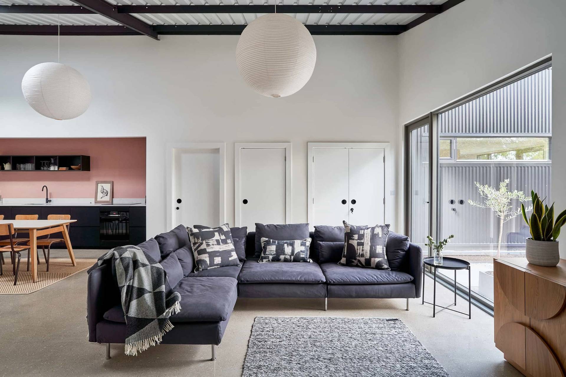 Spacious living room in IP30 with a dark grey corner sectional sofa, white wall panelling, grey area rug, and industrial ceiling beams, Love Locations Suffolk.