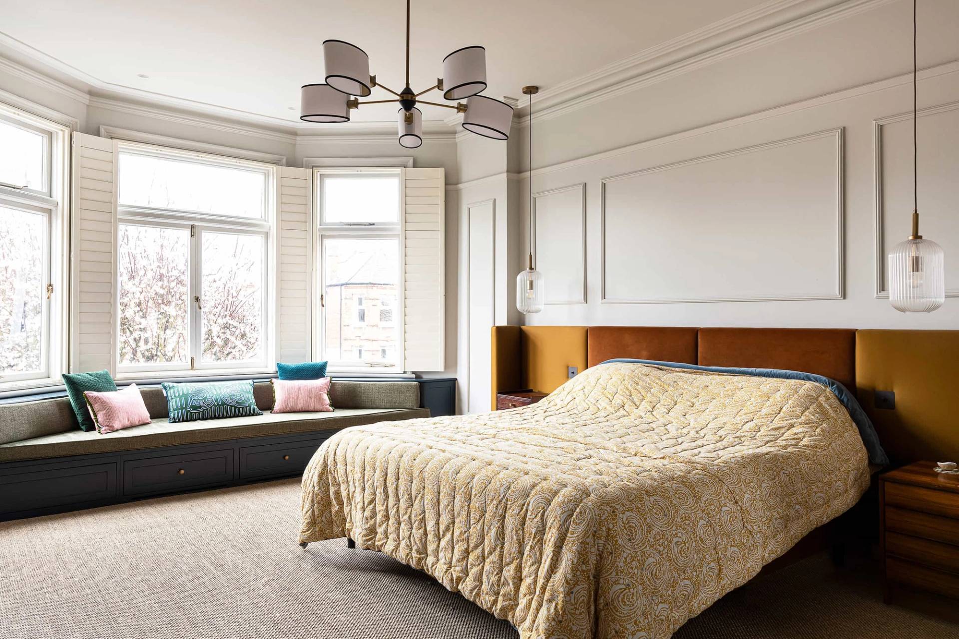 Luxury master bedroom suite featuring a mustard velvet upholstered headboard, window bench, and bay window shutters, perfect for mattress and sleepwear ads, Love Locations.