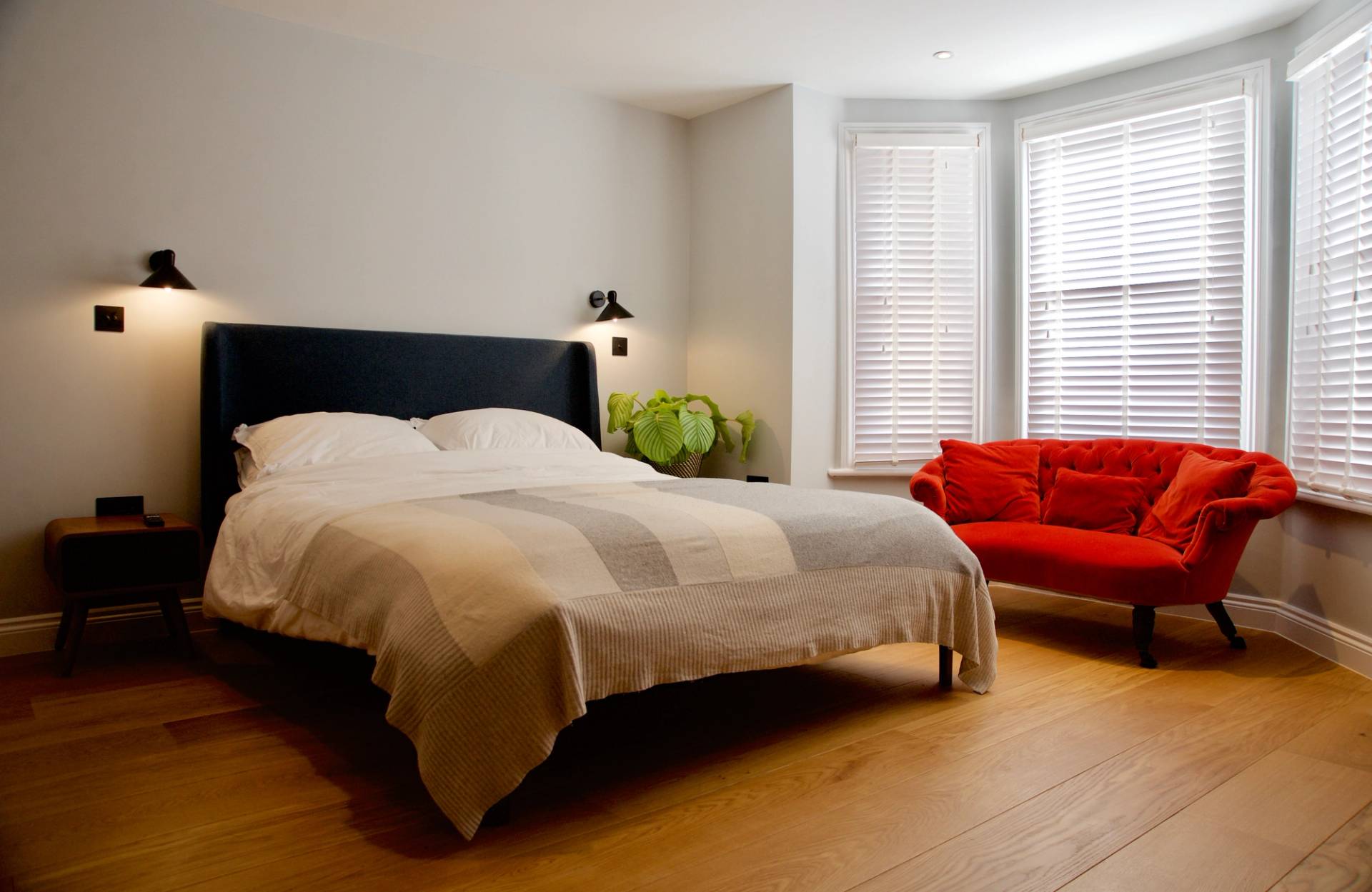 Bright double bedroom featuring a black headboard, red armchair, bay window shutters, and wood flooring, Love Locations TW1.