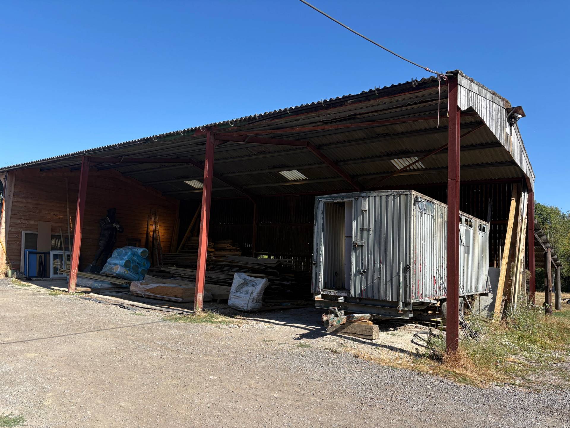 Open-fronted corrugated metal agricultural shed with parked trailer unit, Love Locations BN8.