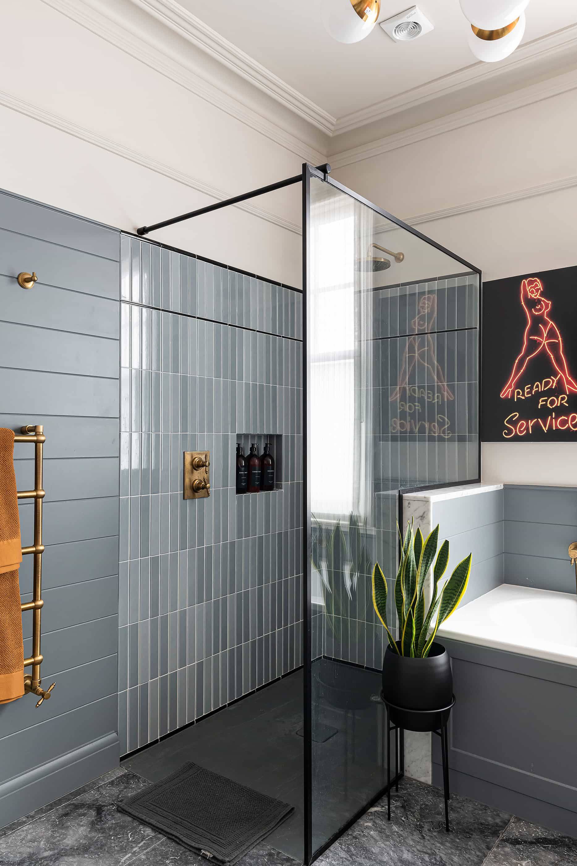 Walk-in shower enclosure featuring vertical grey kit-kat tile walls, brass shower fittings, and glass screen, Love Locations NW6.