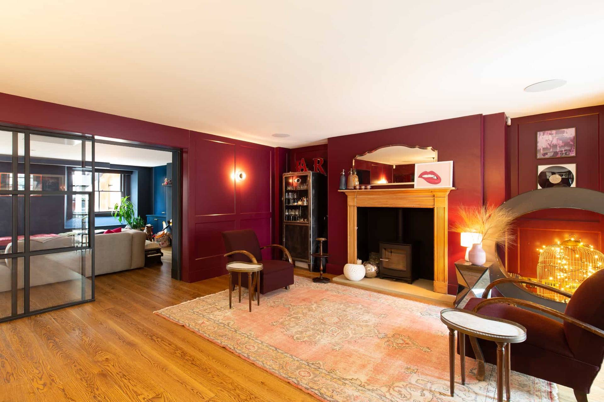 Dark red lounge area with fireplace hearth, wood burner, and open doorway into living space via Love Locations.