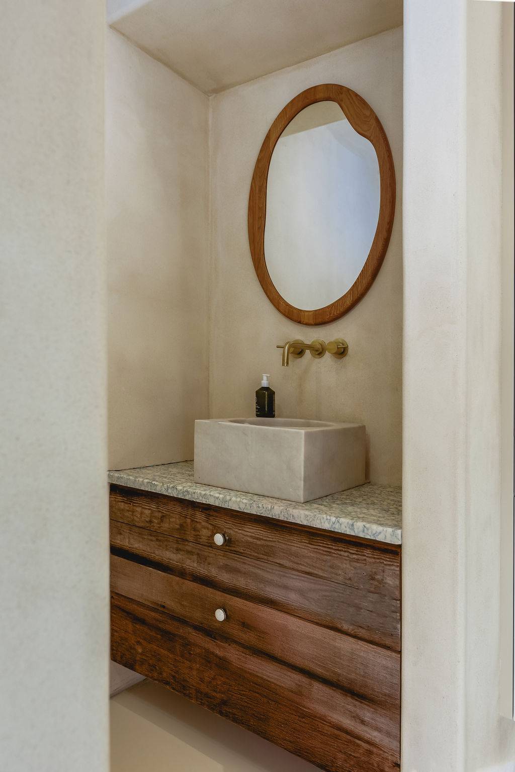 Wooden vanity unit with concrete vessel sink and oval mirror in a neutral microcement bathroom, Love Locations GU32.