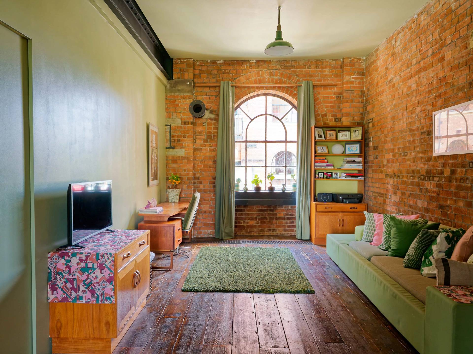 Sunlit loft room with arched window light, exposed red brick walls, and vintage wooden furniture in East London, Love Locations.