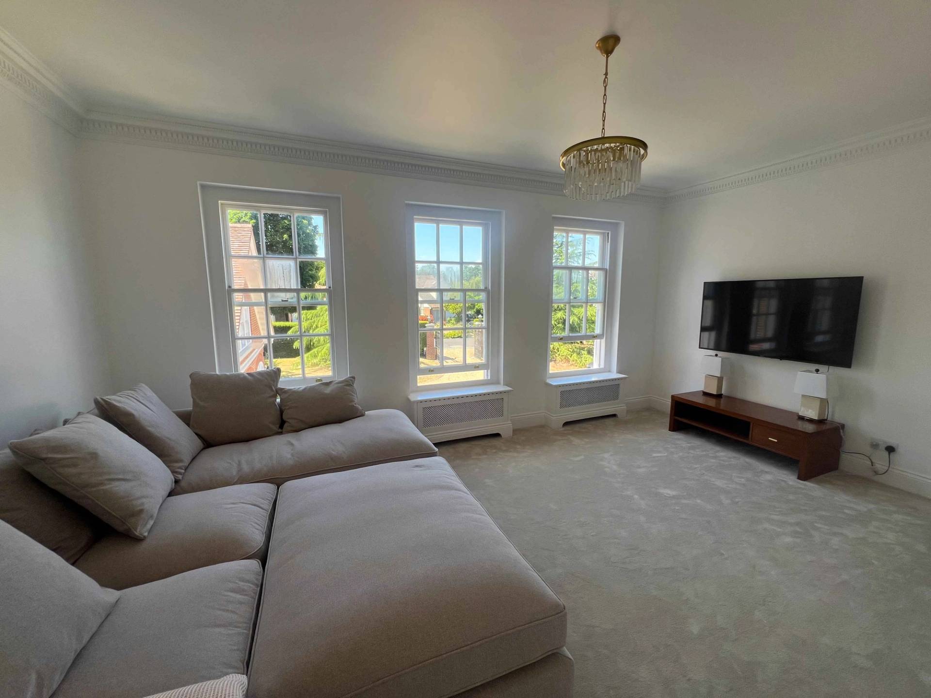 Media room featuring a beige corner sofa and wall-mounted television cast in natural window light, Love Locations BR7.