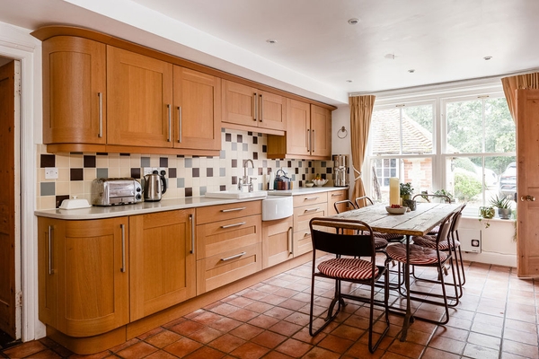 Country style kitchen location house in Liss Hampshire GU33 via Love Locations, featuring natural wood cabinets, a tiled splashback, and a large dining table.