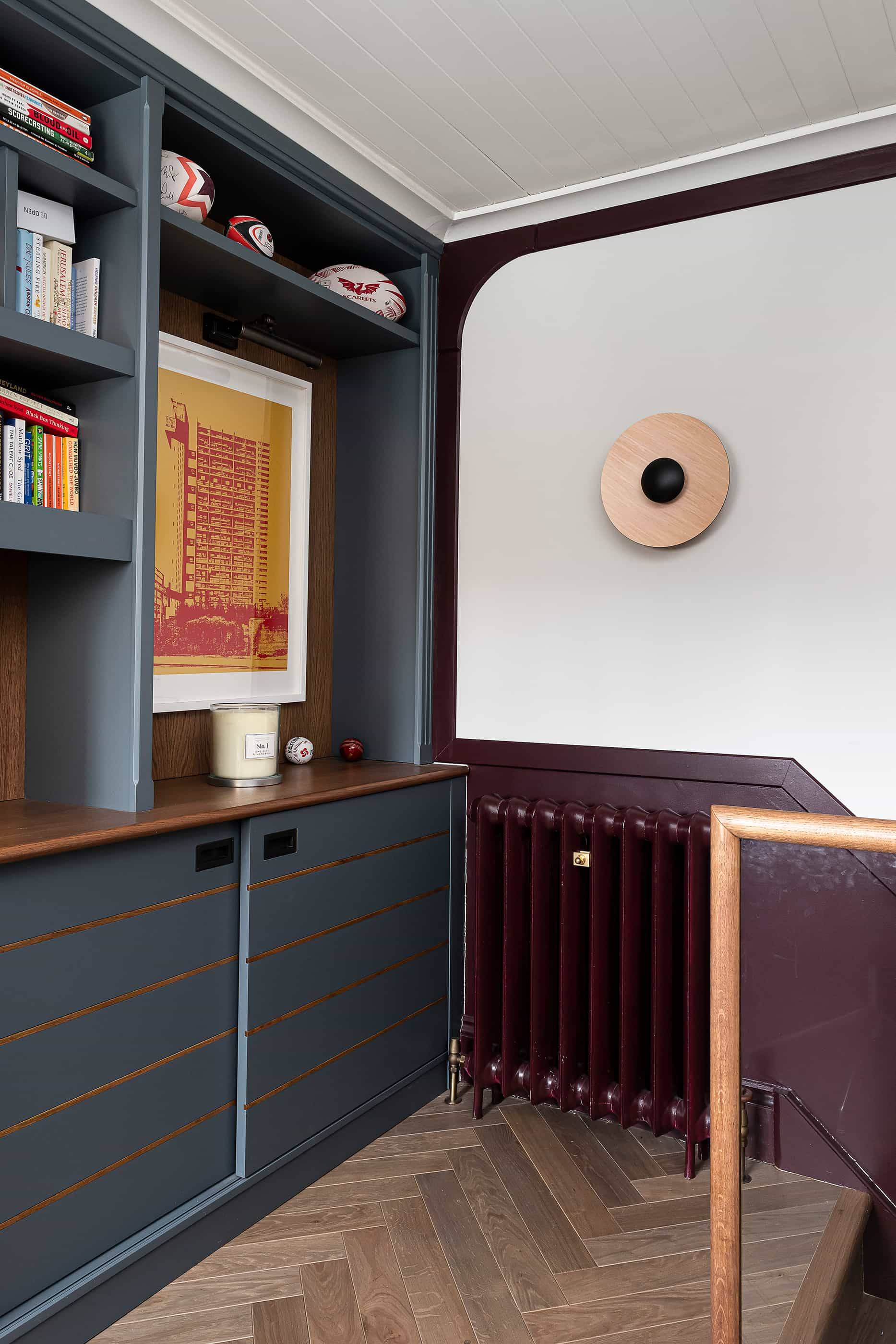 Built-in dark blue dresser cabinet set against burgundy wall panelling with a circular wall sconce, Love Locations NW6.