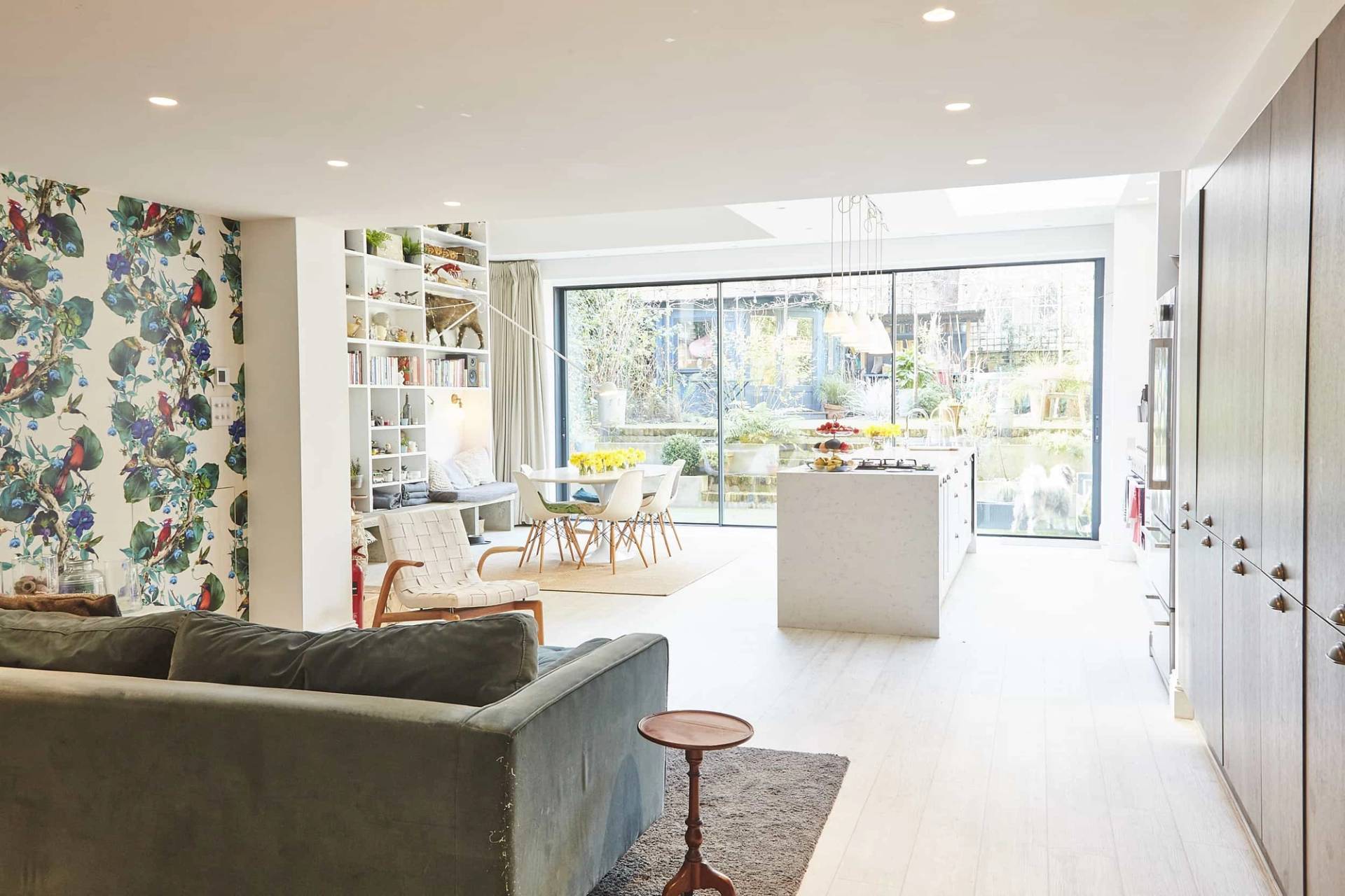 Spacious open-plan living and kitchen area looking toward a dark green velvet sofa and floor-to-ceiling glass doors, Love Locations.