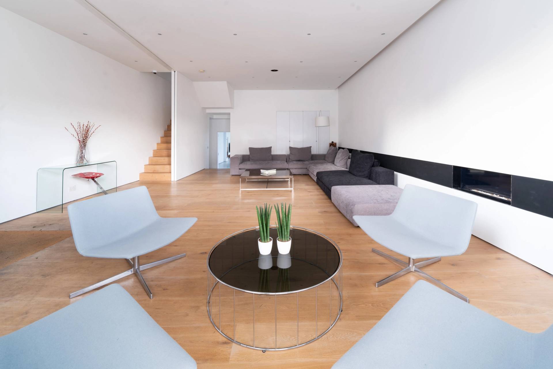 Contemporary reception lounge with low-profile chairs, circular glass coffee table, and wood flooring in Fulham, Love Locations SW6.