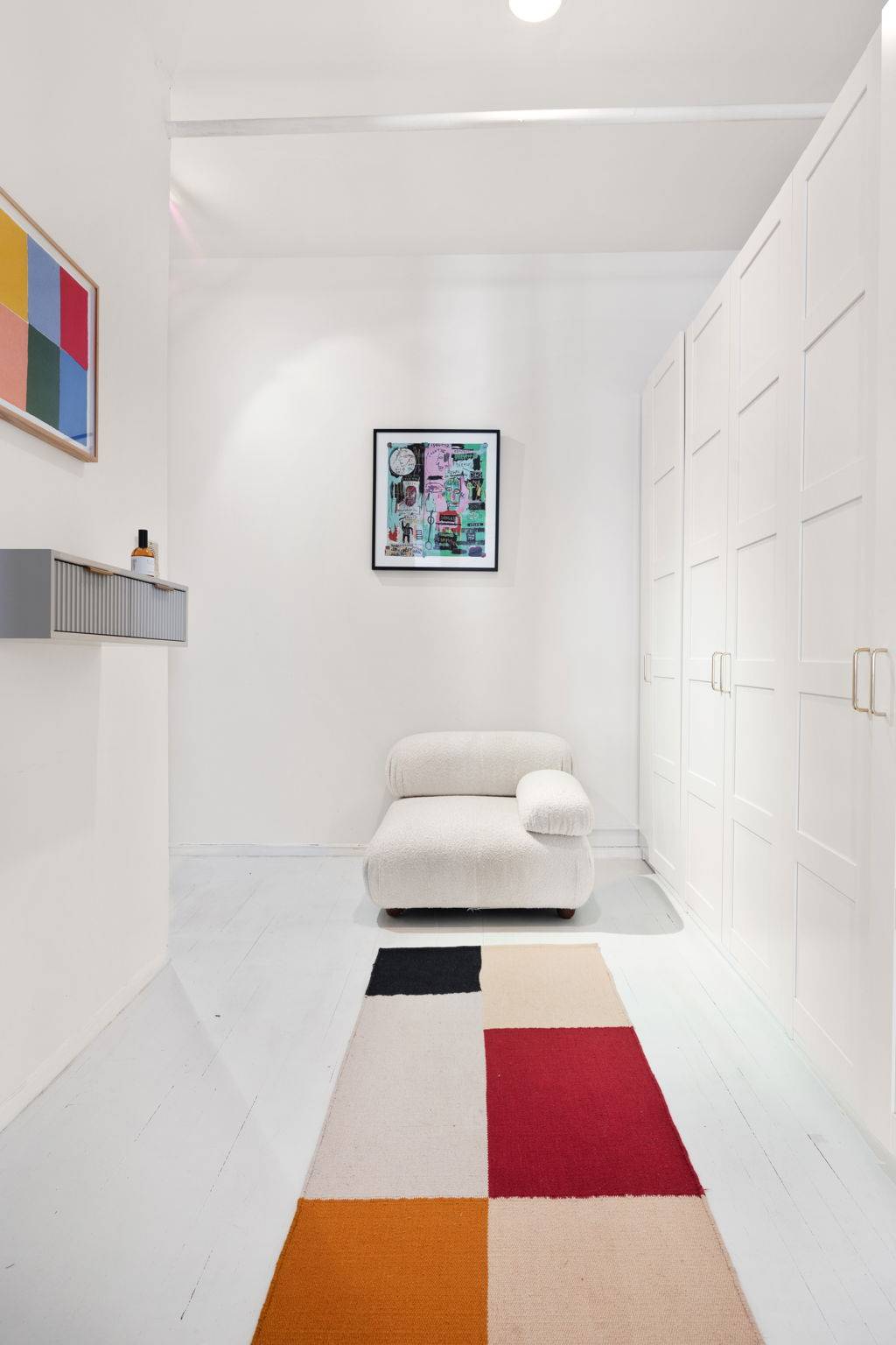 Minimalist white gallery hallway with built-in white wardrobe closets, cream armchair, and geometric floor rug in a Tribeca NY 10007 loft location through Love Locations.