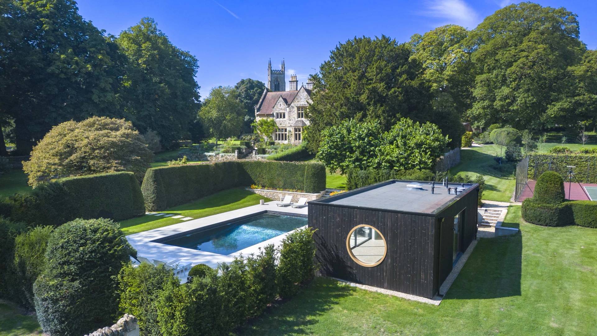 Aerial drone view of a black modern pool house, outdoor swimming pool, and Cotswold manor estate, Love Locations OX7.
