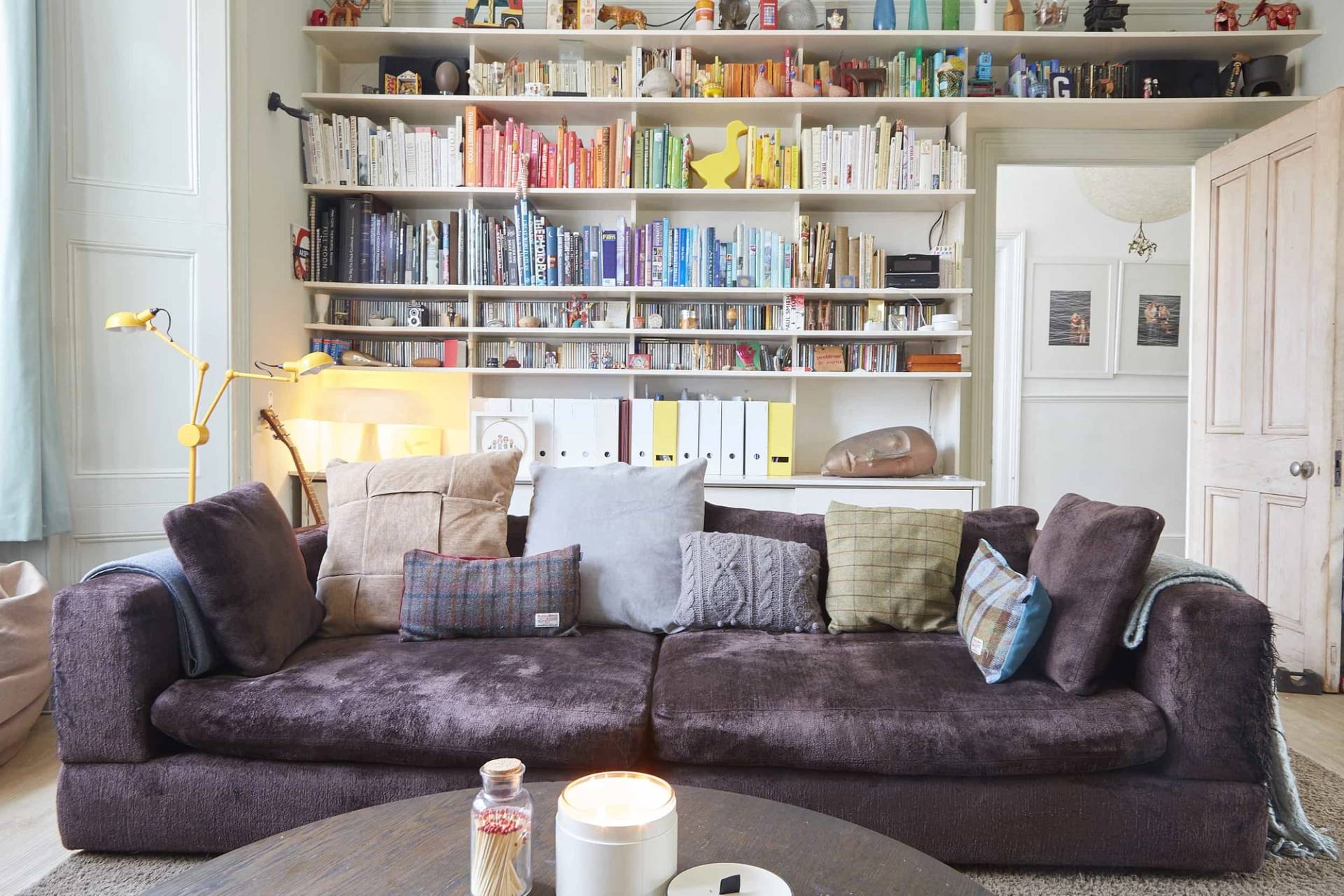 Cozy TV lounge area featuring a full-wall white bookcase, dark brown sectional sofa, and warm ambient lighting, Love Locations N5.