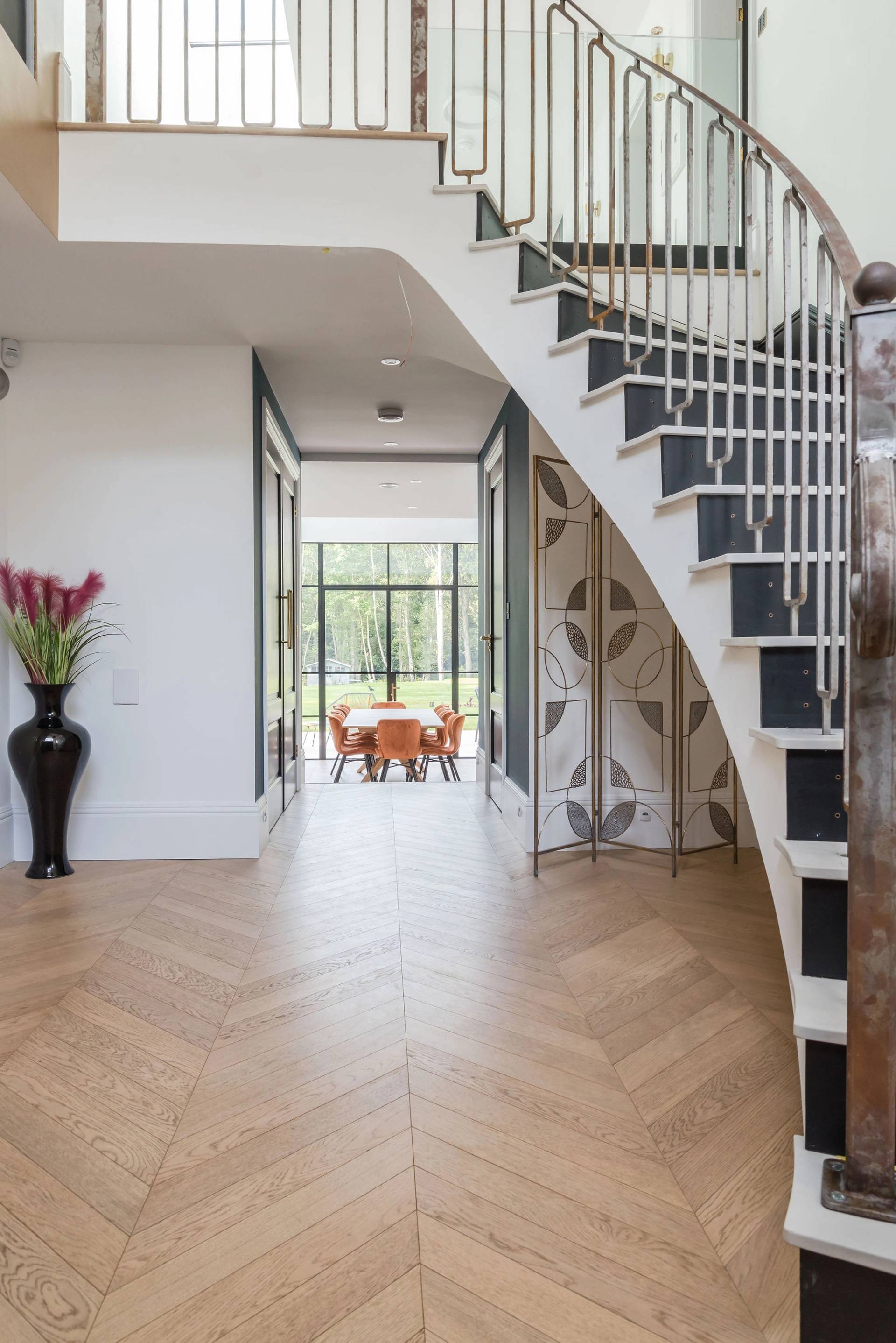 Curved white metal spiral staircase set on herringbone oak flooring in a modern luxury mansion, Love Locations GU3.