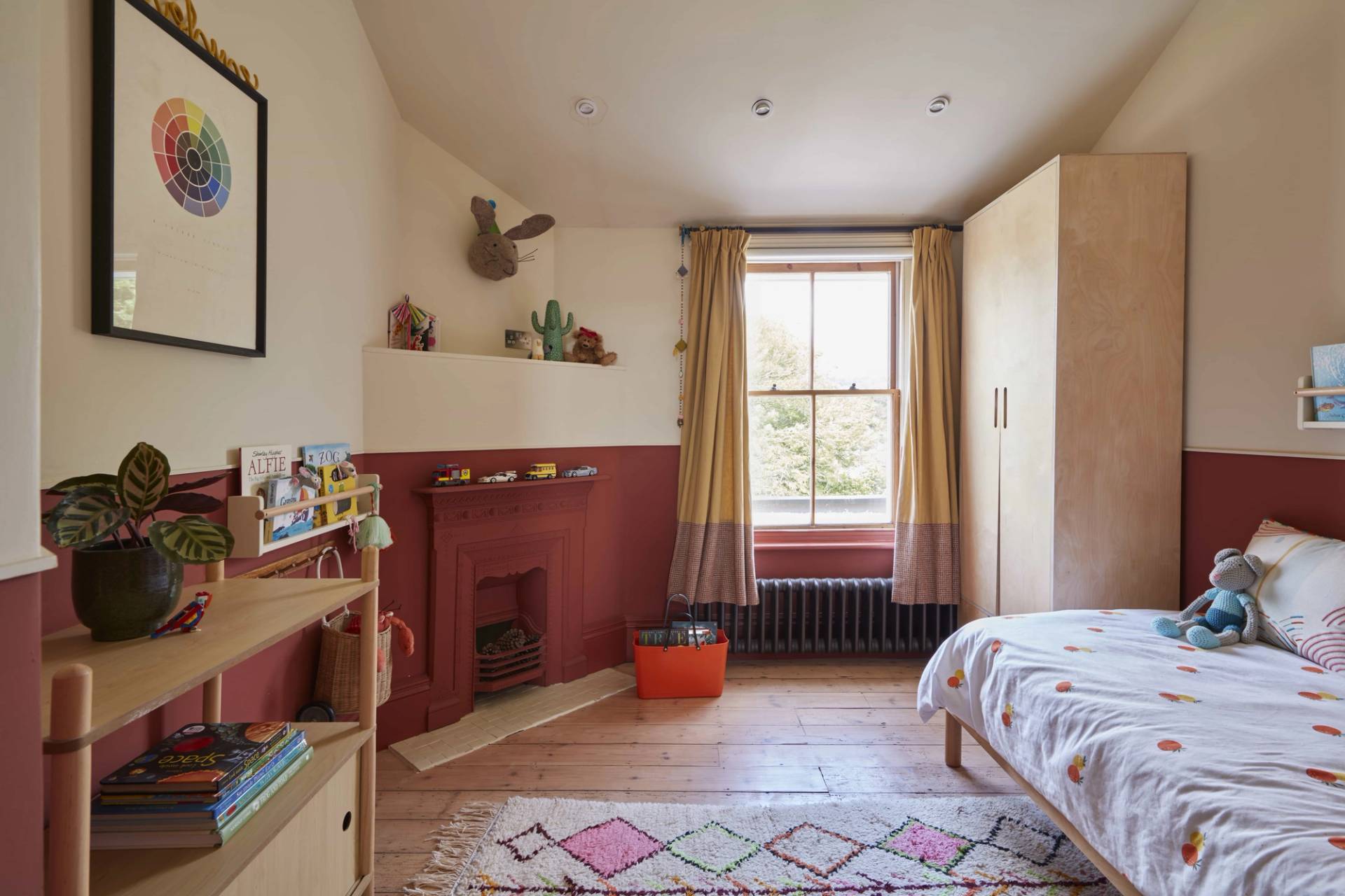 Children's bedroom featuring terracotta red lower wall paint, built-in shelving, and colorful styling, ideal for family brand advertising, Love Locations.