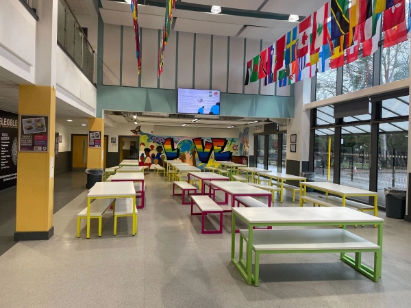 Love Locations large school canteen shoot location Reading RG30: Open plan dining hall with colorful bench tables and international flags, ideal for institutional filming, TV dramas, and commercial shoots.