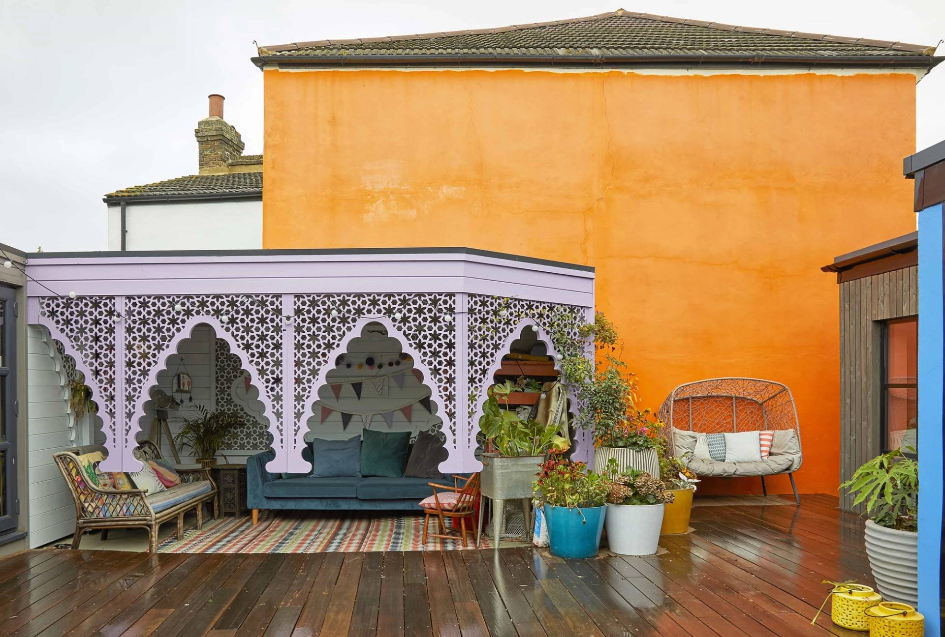 Carved purple wooden veranda arch set against an orange house facade on a wet timber deck, Love Locations Catford.