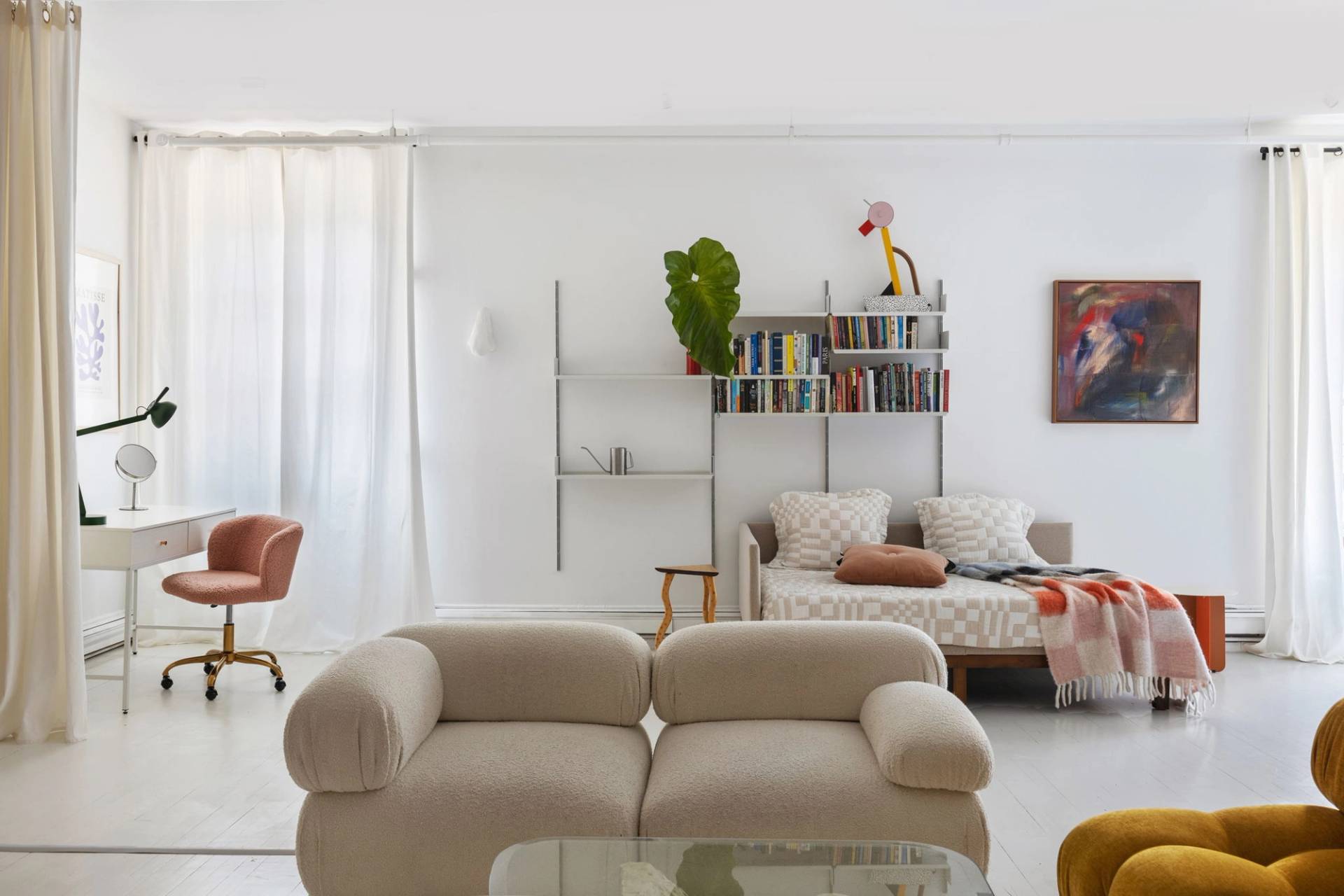 Cozy lounge nook with a cream velvet sofa, glass table, and minimalist shelving unit in a Tribeca NY loft location house by Love Locations.