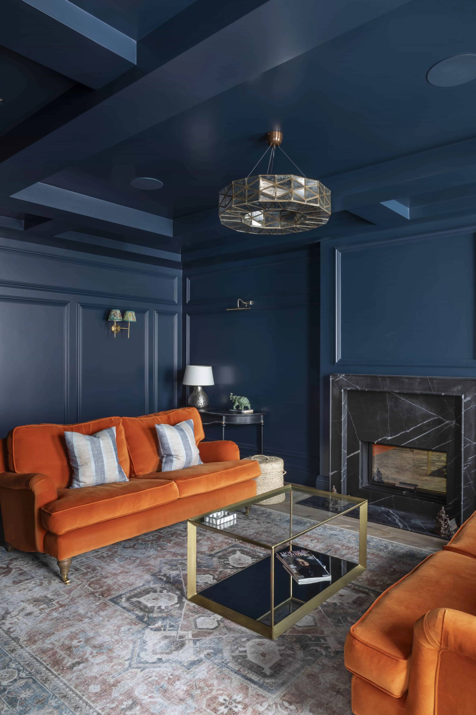 Moody dark navy reception room featuring an orange velvet sofa, inset fireplace, and gold coffee table, Love Locations HP18.