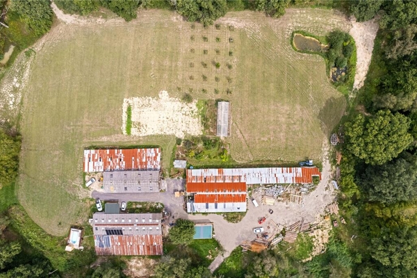 Top-down aerial drone view of industrial farm outbuildings, greenhouses, and rusty corrugated roofs, Love Locations BN8.