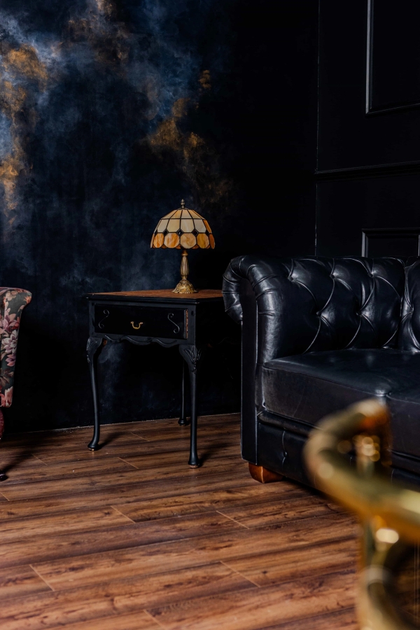 Classic black panelled wall studio set with a black leather chesterfield couch and antique side table, Love Locations N15.