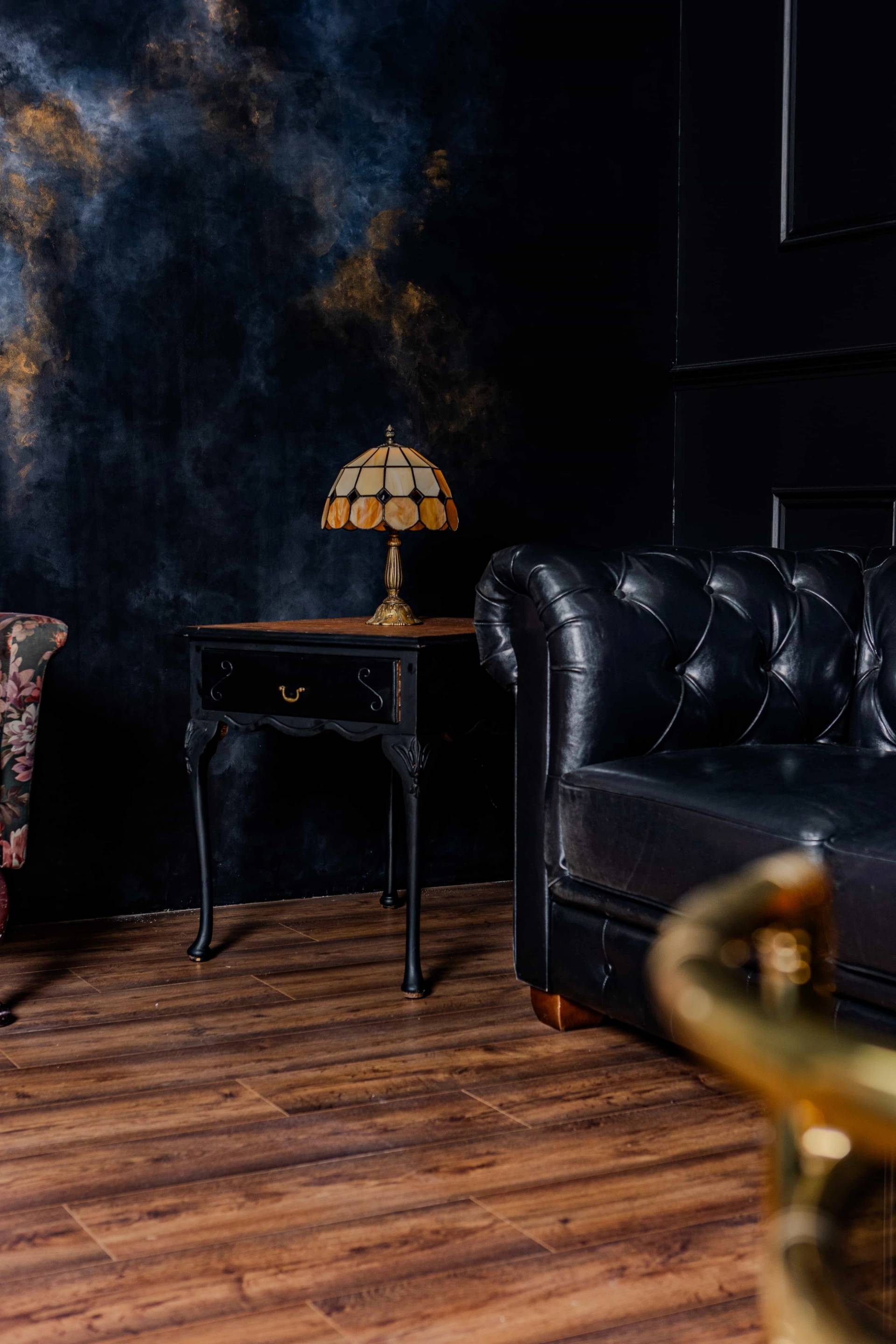 Classic black panelled wall studio set with a black leather chesterfield couch and antique side table, Love Locations N15.