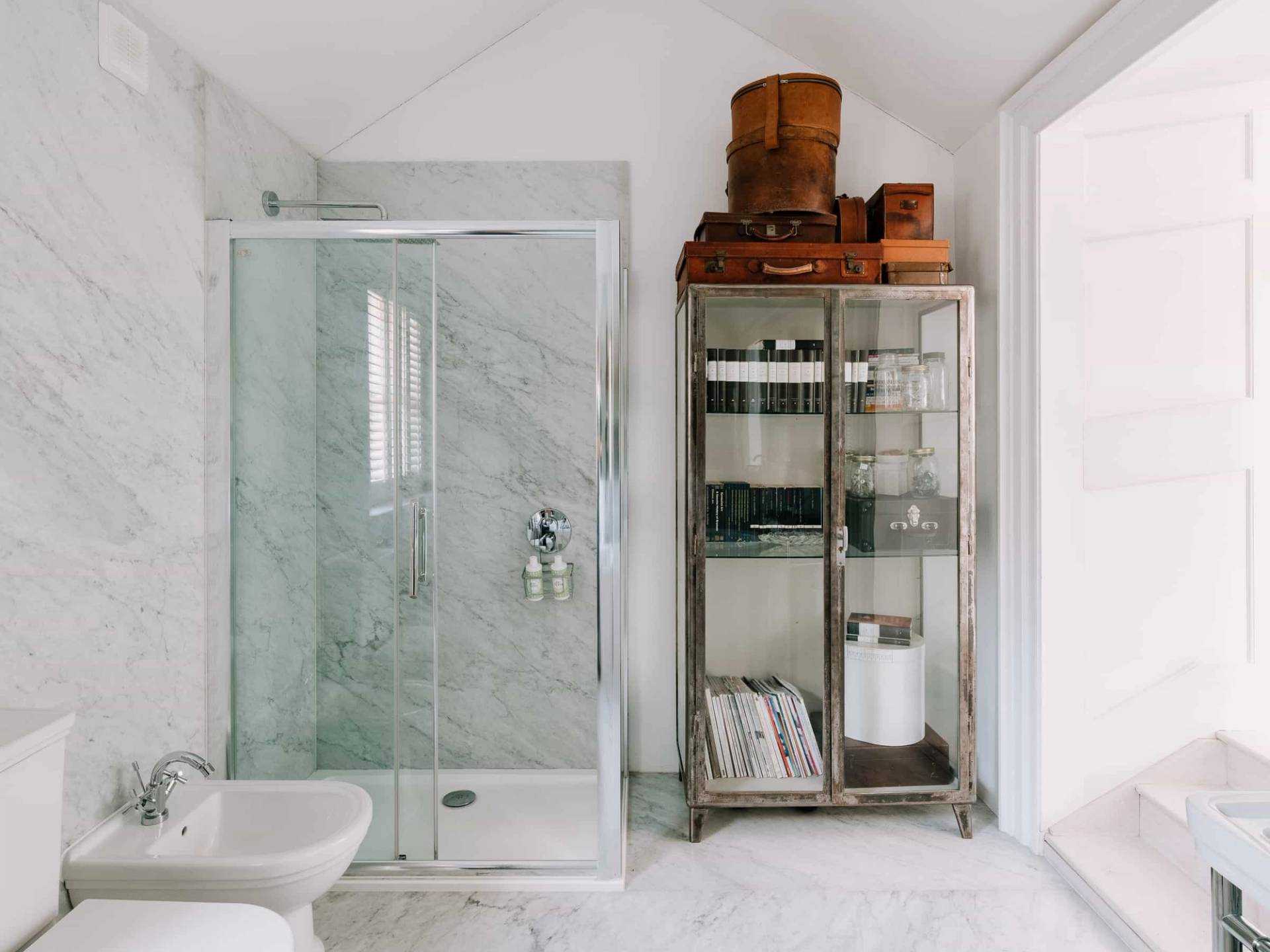 Modern bathroom with a glass walk-in shower enclosure, freestanding glass cabinet, and marble tiles, Love Locations RG42.