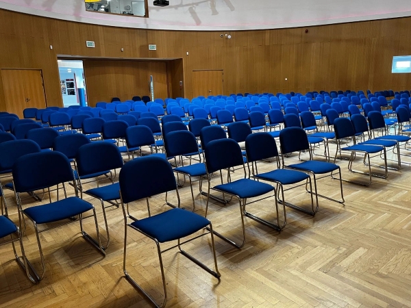 Love Locations school assembly hall London SE2: Deep perspective shot of blue auditorium seating on a classic herringbone parquet floor, excellent for institutional presentations and drama filming.