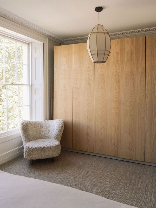 Custom floor-to-ceiling light wood wardrobe storage wall paired with a cozy bouclé armchair, Love Locations.
