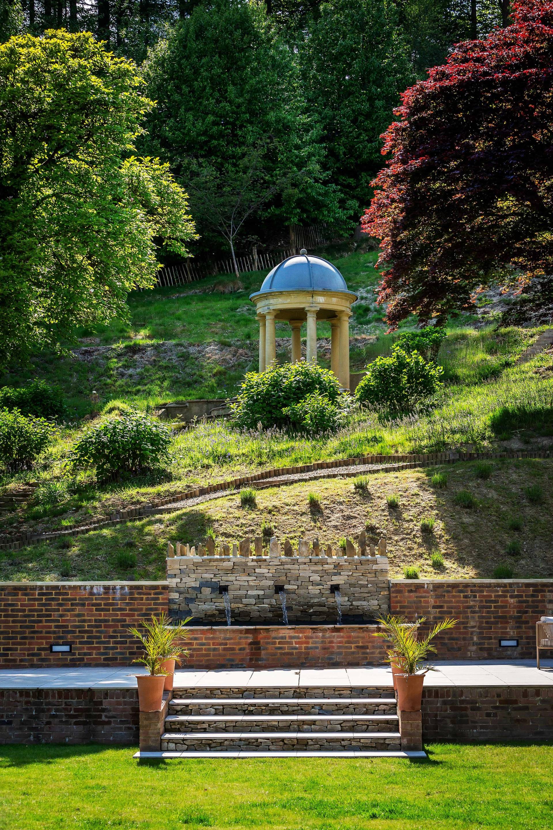 Italianate stone water feature fountain set on a terraced garden hill with a classical pavilion dome, ideal for high-fashion editorial photography, Love Locations GU27.