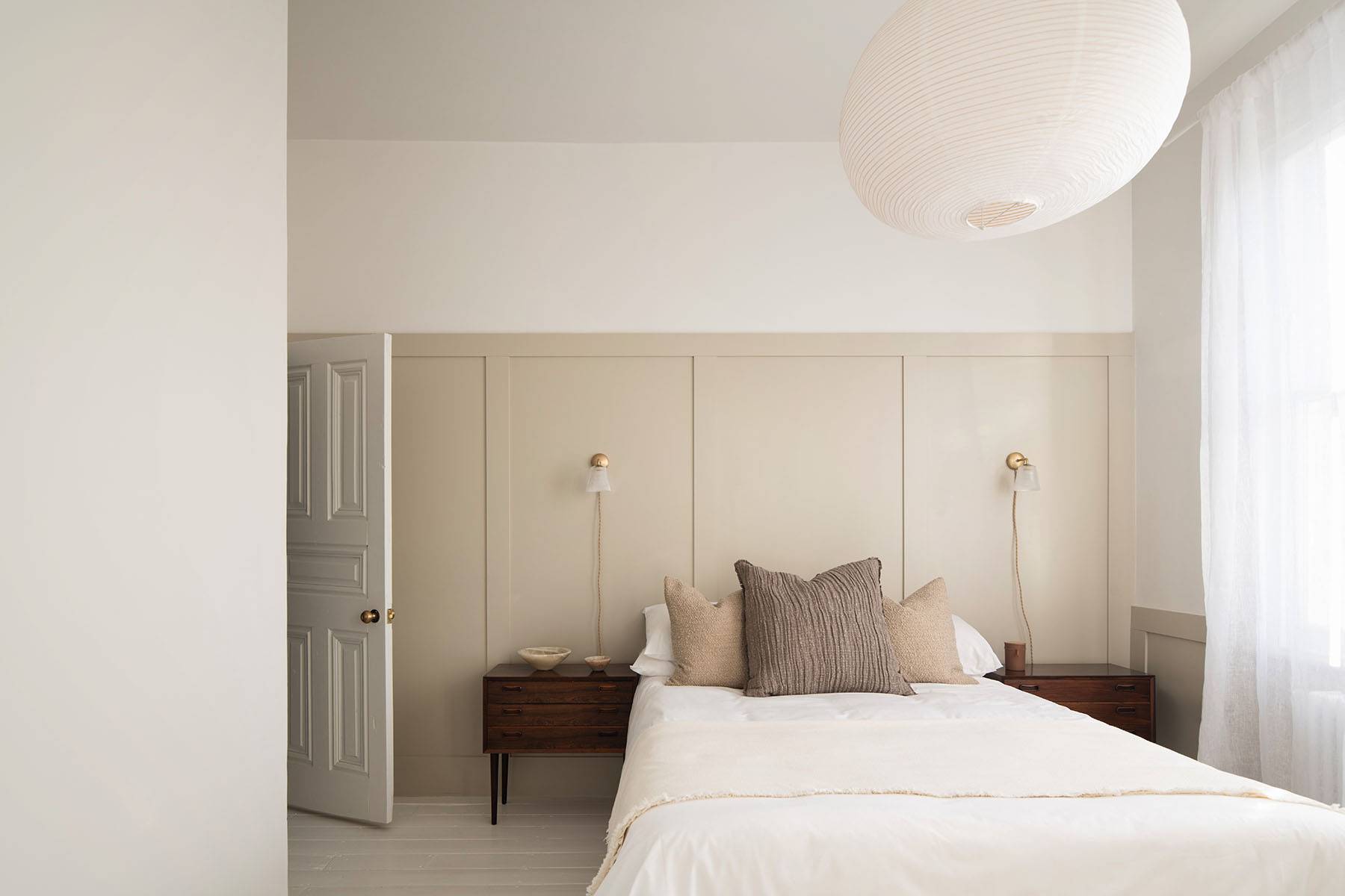 Cozy bedroom suite with sheer white window curtains, warm neutral walls, and large floor plant, ideal for bedding ads, Love Locations SW16.