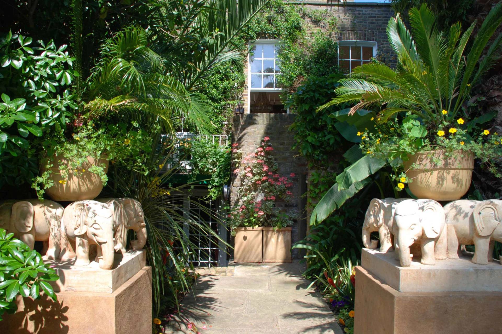 Grand luxury townhouse shoot location hero cover image in Kensington and Chelsea, SW5 featuring carved stone elephant entrance pillars, lush tropical palm gardens, a private outdoor swimming pool, scenic mural dining rooms, and crystal chandeliers, the ultimate high-visibility backdrop for feature film productions, luxury brand campaigns, TV period dramas, and high-fashion editorials via Love Locations.