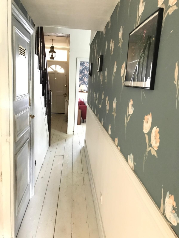 Long residential entrance hallway showing worn white timber floorboards and pale green patterned wallpaper, suitable for realistic TV drama filming, Love Locations.