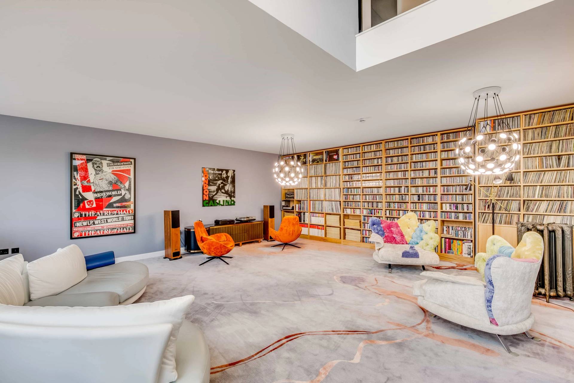 Library sitting room featuring a massive wall of books, orange lounge chairs, and curved white sofa, Love Locations CB2.