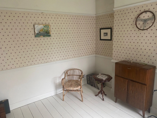 Bright, minimalist room corner styled with a retro wicker chair, vintage side table, and textured wallpaper, perfect for character-driven interview setups, Love Locations.