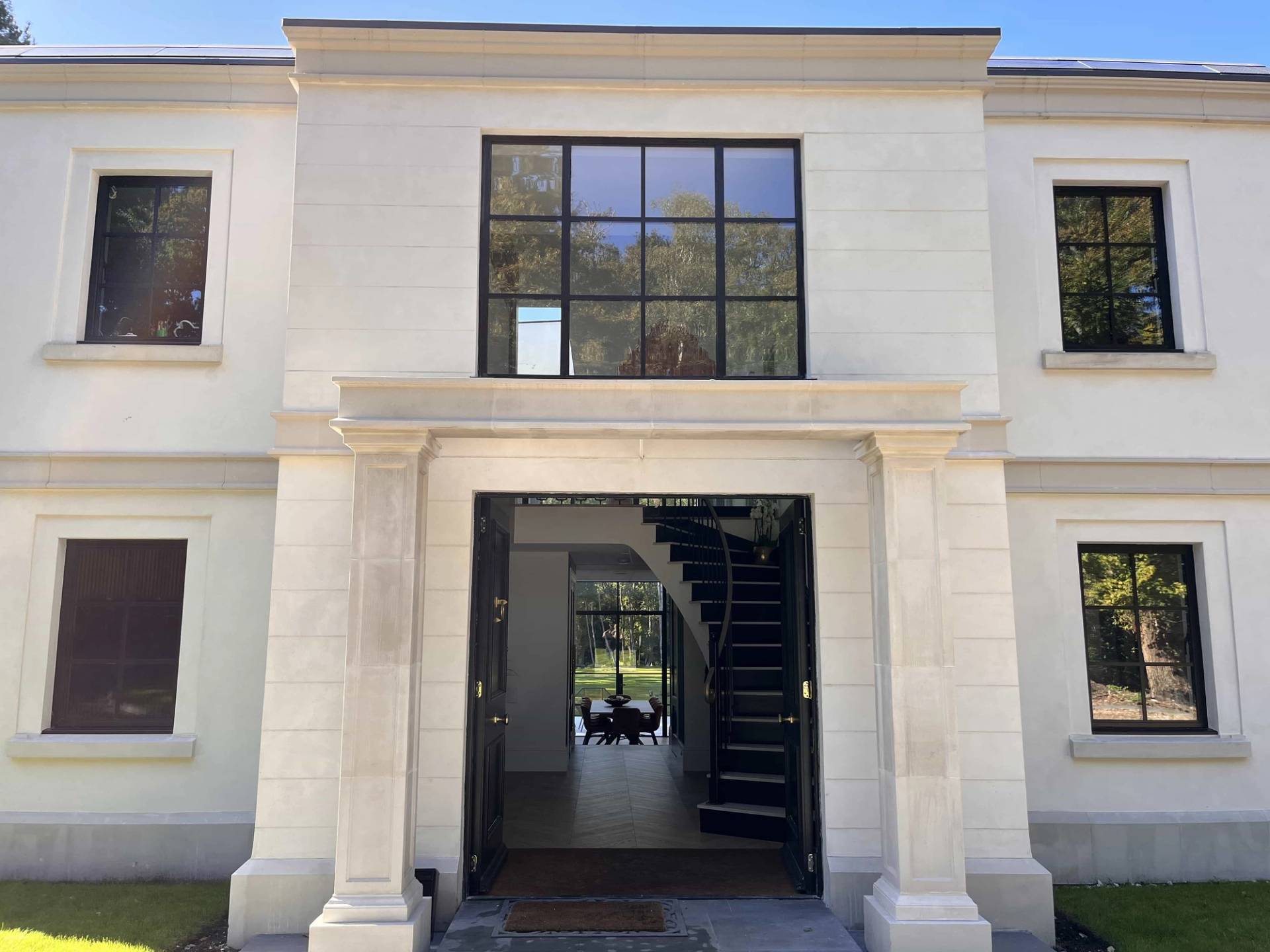 Grand stone entrance portico of a white mansion with double black entry doors, Love Locations GU3.