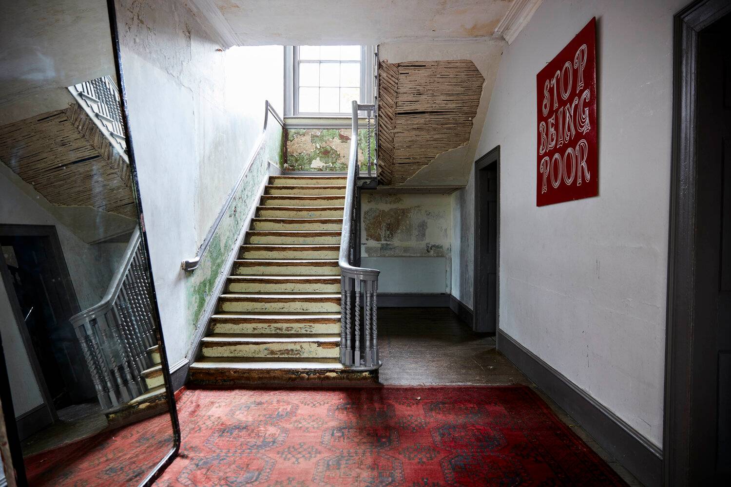 Atmospheric derelict hallway and grand wooden staircase with red carpet runner and distressed plaster walls, ideal for music video shoots, Love Locations SE8.