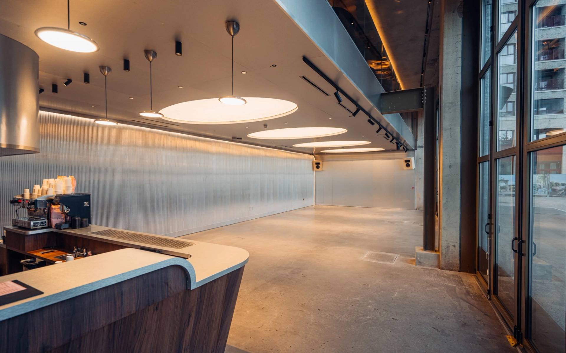 Modernist bar and lounge interior with a wooden serving counter and circular ceiling light installations via Love Locations.