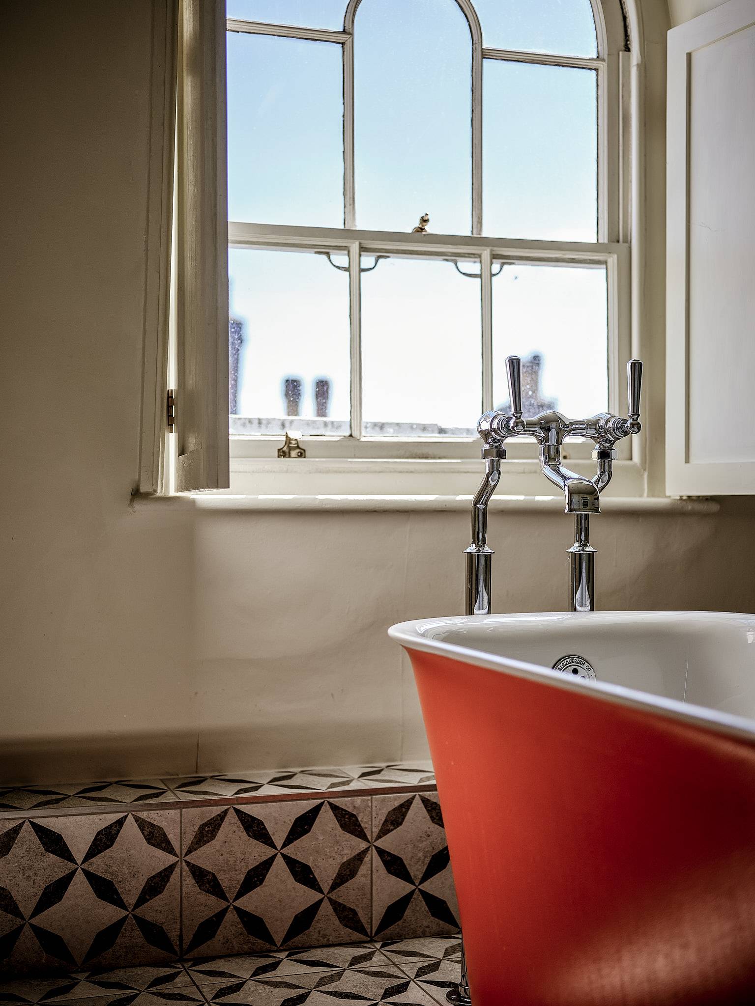Close-up detail of a terracotta bath tub set beside a sash window with brass tapware, Love Locations.