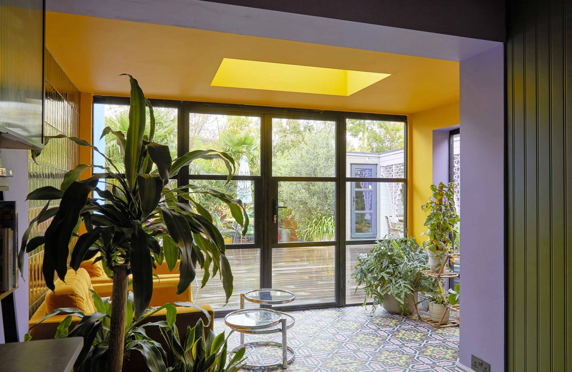 Sunlit sunroom lounge with full-height black sliding glass doors opening onto an outdoor garden deck, Love Locations Catford.