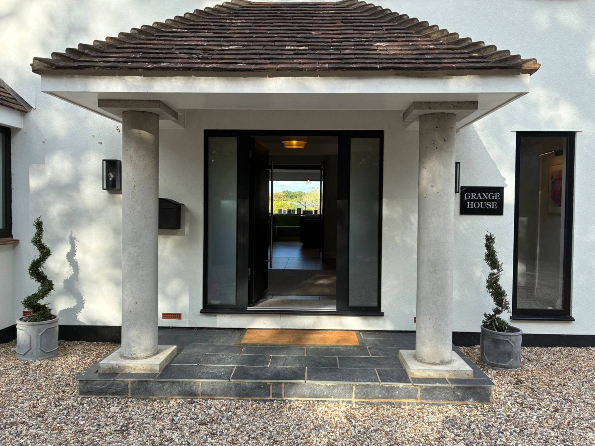 Covered front porch entrance exterior of a modern country house in Essex CM4 from Love Locations, featuring stone pillars and a dark wood front door.