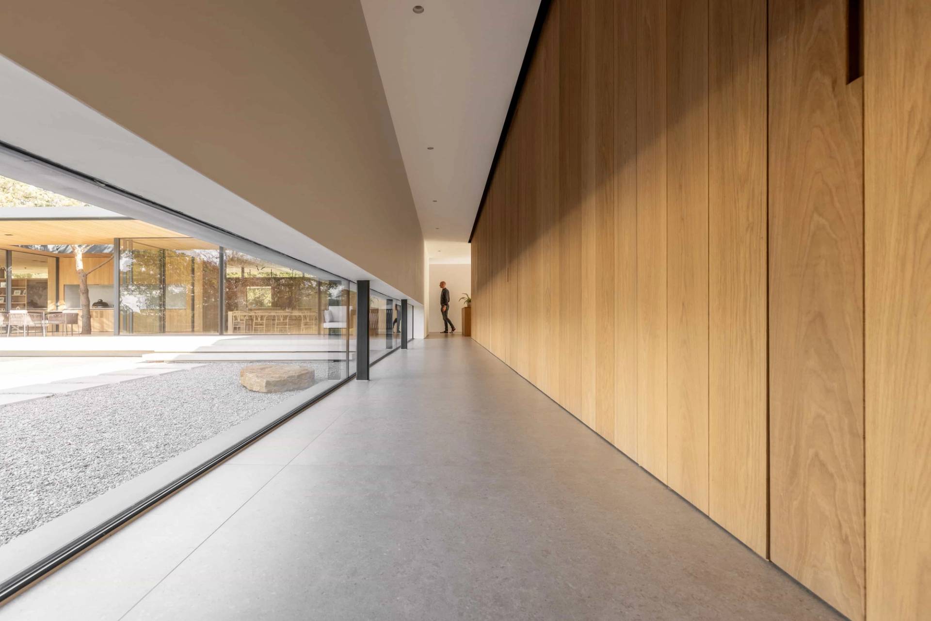 Long architectural hallway corridor featuring linear wood wall panelling, polished floors, and a continuous row of low-level glazing, Love Locations CM4.