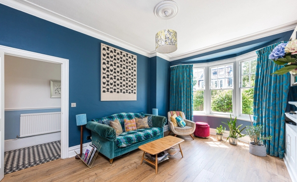 Stunning formal living room with deep blue walls, a teal velvet sofa, and a large Edwardian bay window, via Love Locations Barnet.