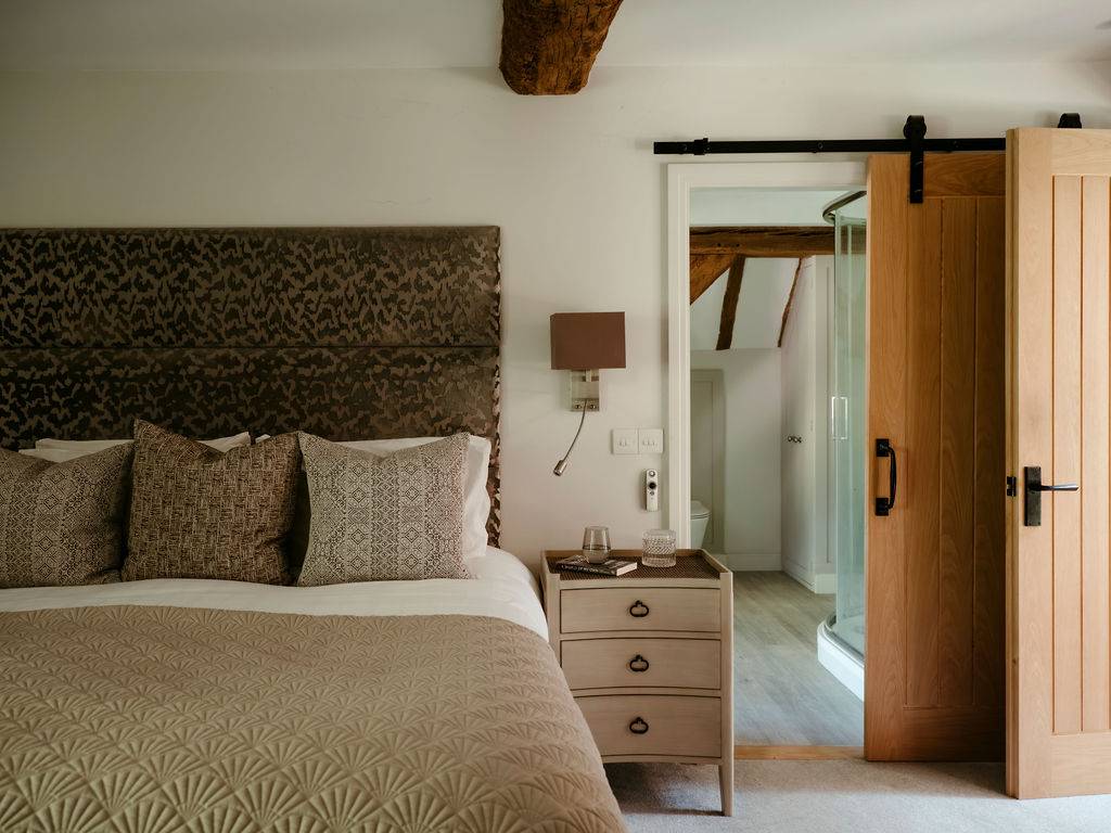 Country bedroom setup showing a sliding barn door partition and a custom upholstered headboard, ideal for sleepwear campaigns, Love Locations.