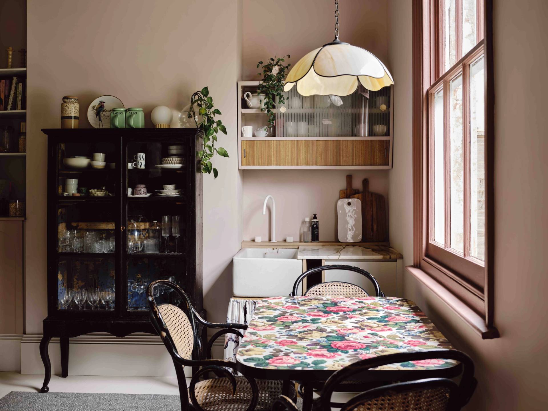 Cozy kitchen dining nook featuring a floral oilcloth table, black bistro chairs, and dark china cabinet, Love Locations CR0.