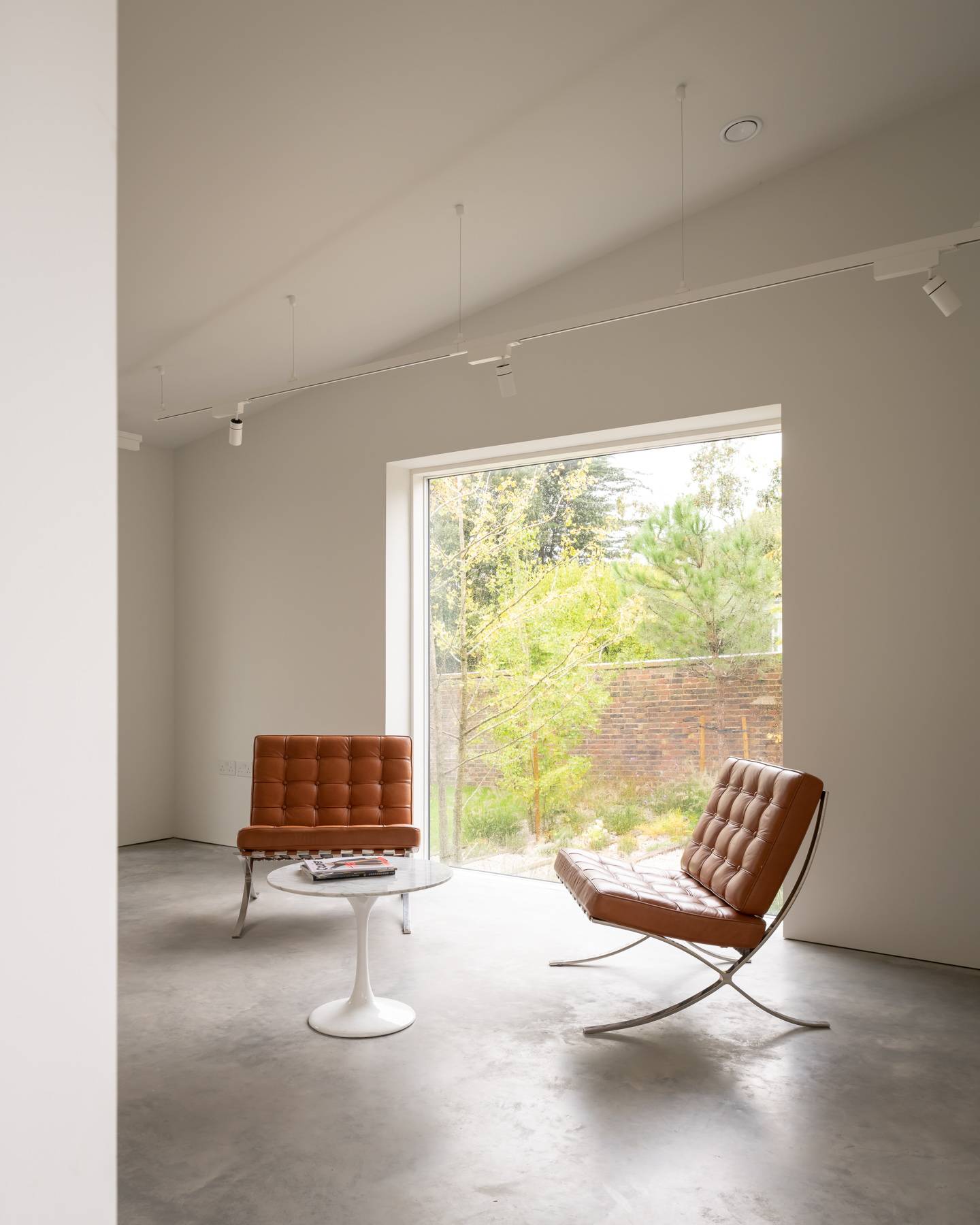 Cognac leather Barcelona armchairs set in a sunlit white gallery room with picture window light, Love Locations BN3.