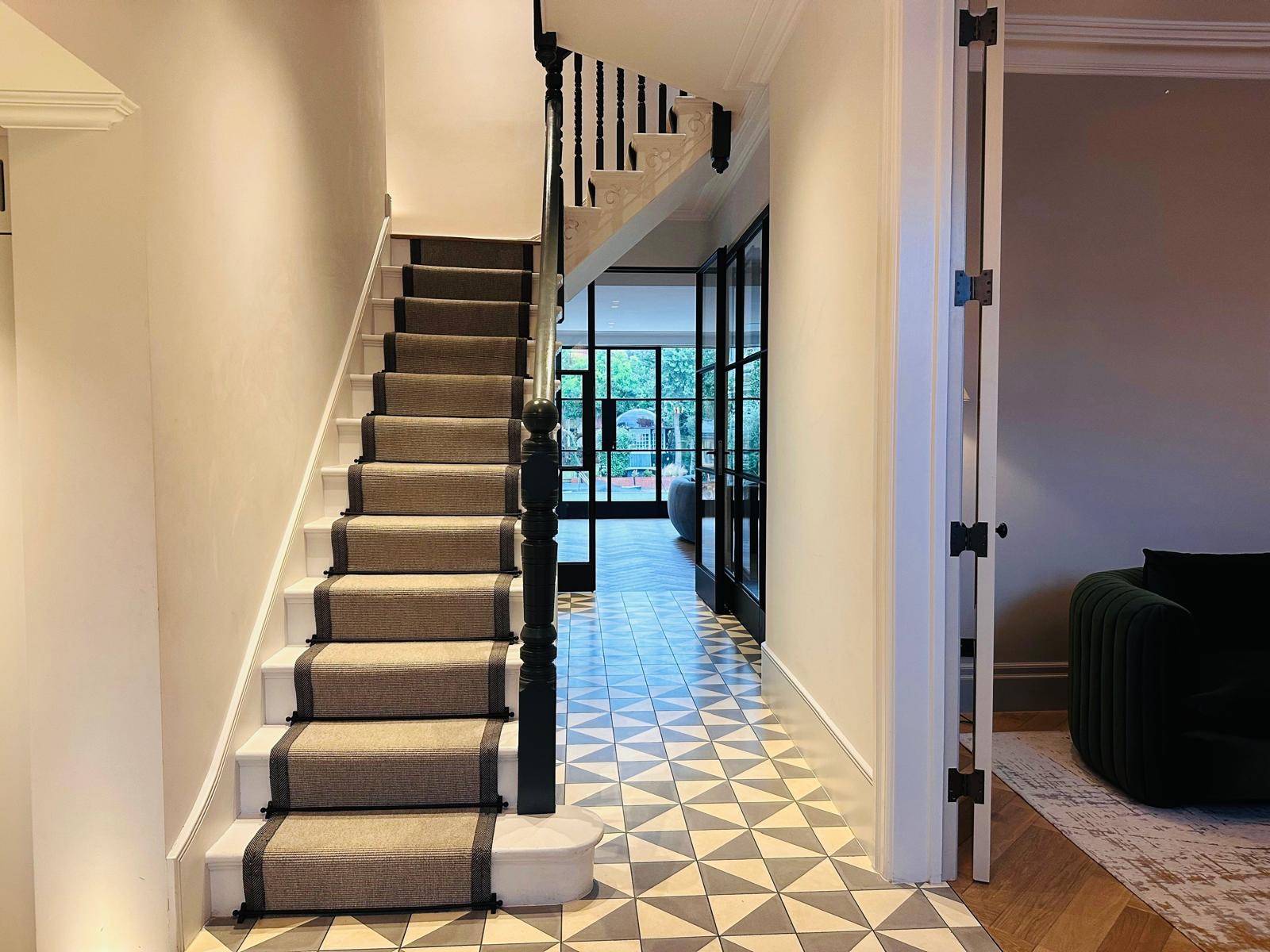 Victorian staircase hallway with grey carpet runner, black balustrade, and geometric floor tiles, Love Locations TW11.