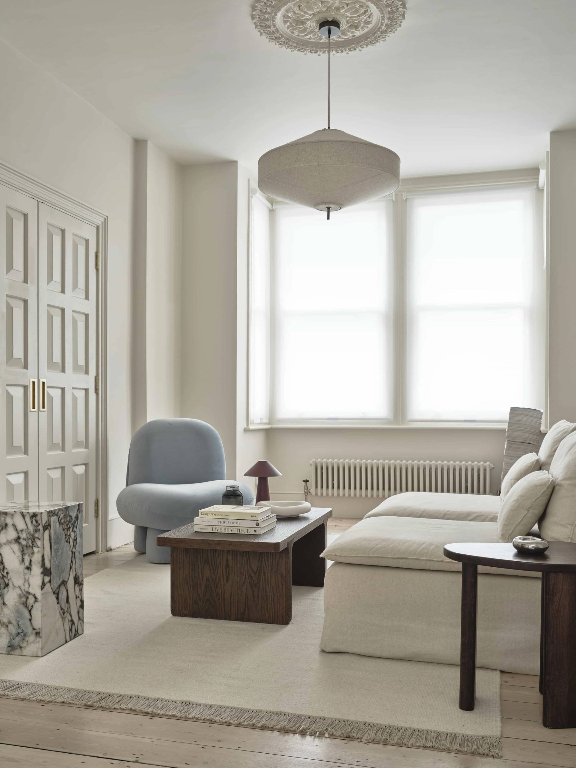 Editorial living room layout featuring a plush cream sofa, curved light blue armchair, and dark wood coffee table, Love Locations E4.