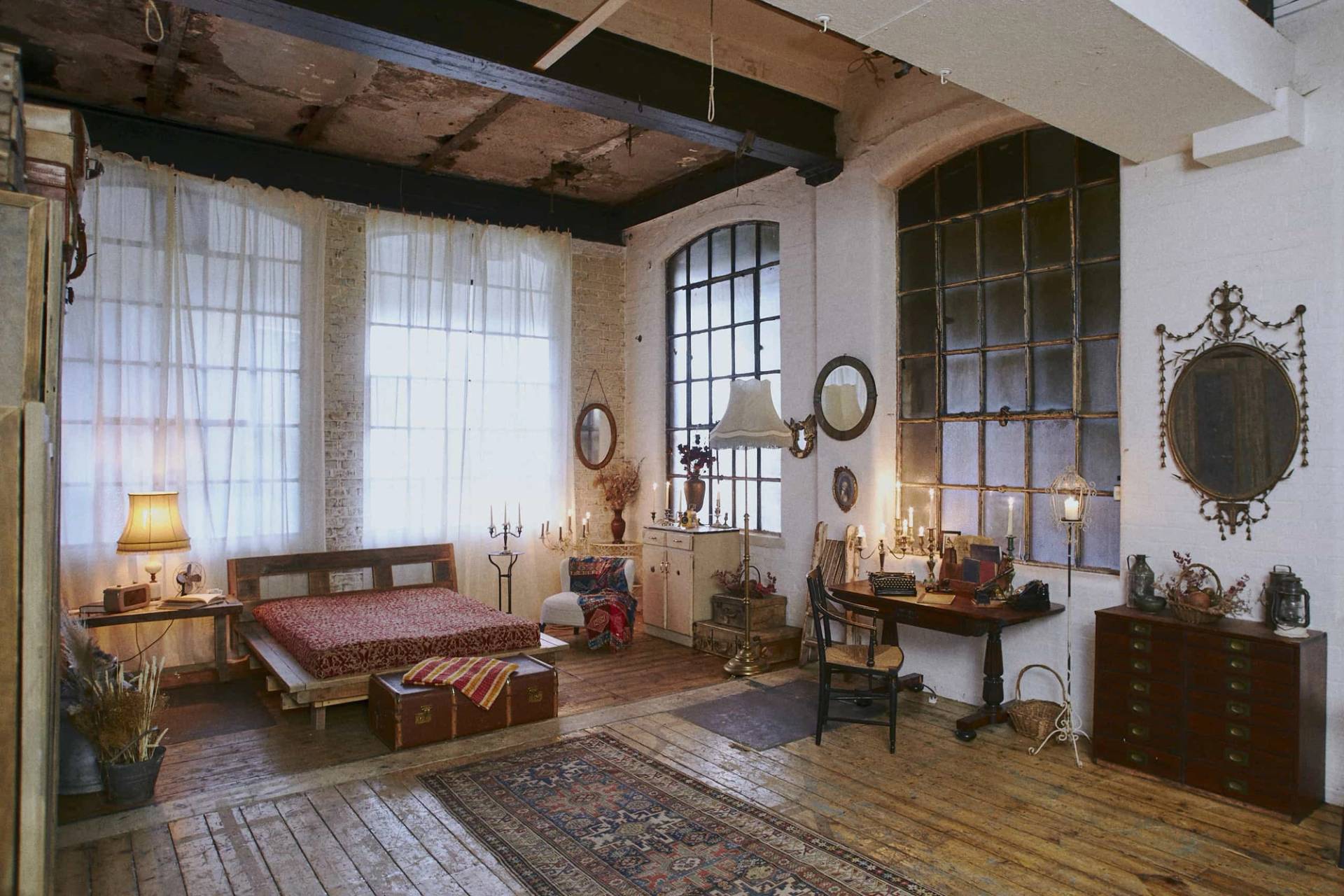 Wide shot of an industrial loft bedroom setup complete with rustic furniture, candles, and factory window backdrops for film sets, Love Locations EN5.