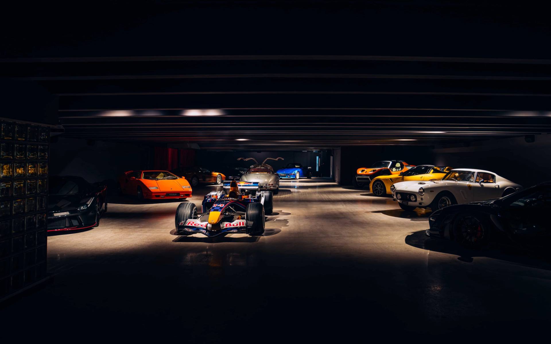 Atmospheric view of a Formula 1 race car and classic sports cars illuminated beneath spotlighting in a dark concrete vault in Brentford TW8 from Love Locations.